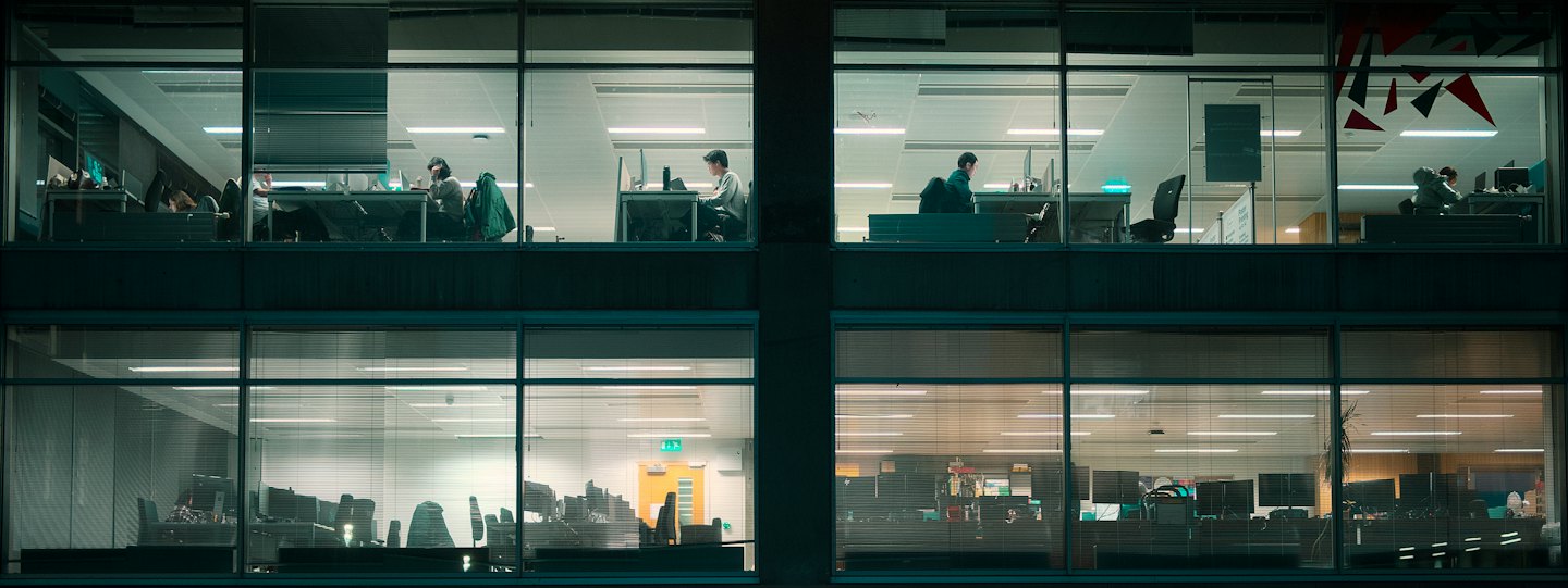 Professionals working at desks inside an illuminated modern office building.