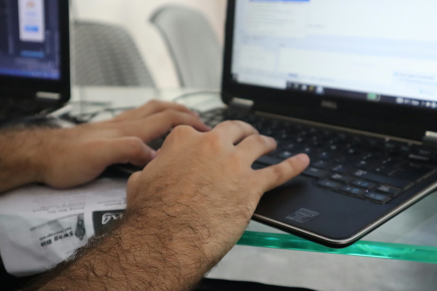 Hands typing on a laptop keyboard at a glass desk.